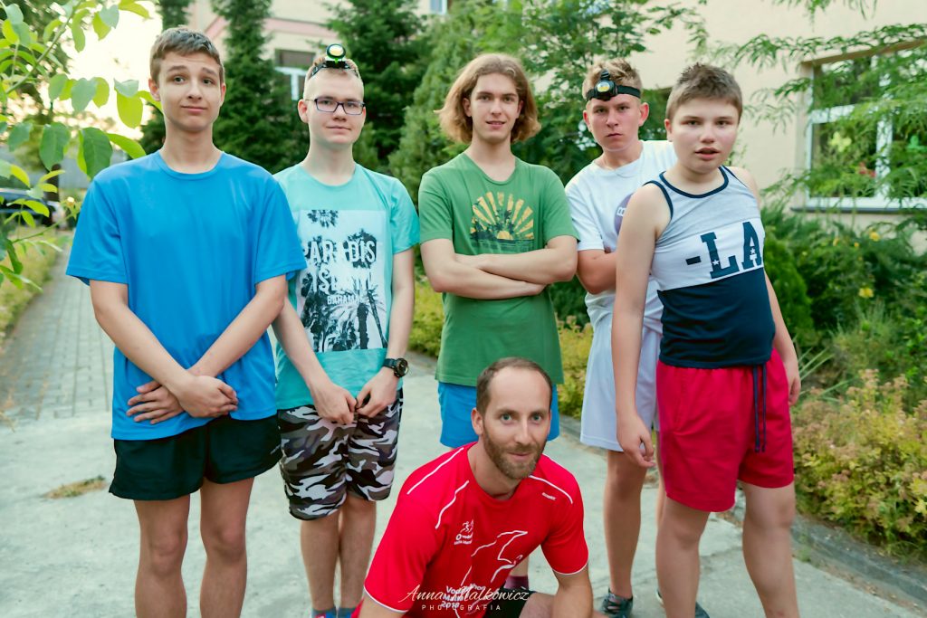 Grupa chłopców z opiekunem ubranych w sportowe stroje biegowe i czołówki. 